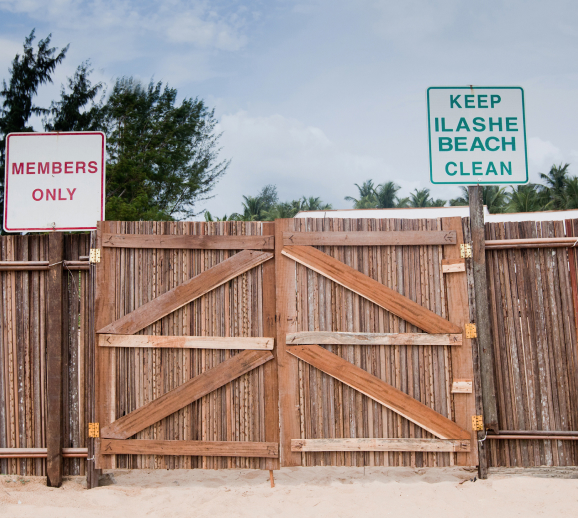 A wooden gate designed by Oshinowo Studio, on a sandy beach with signs that read "members only" and "keep Ilashe Beach clean".