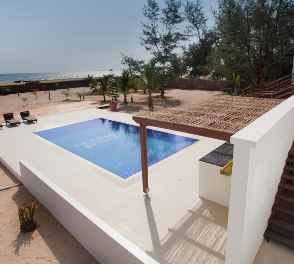 A tranquil poolside retreat by the beach, designed by the leading architectural design studio in Lagos, Oshinowo Studio, features a thatched-roof relaxation area and a glimpse of the ocean in