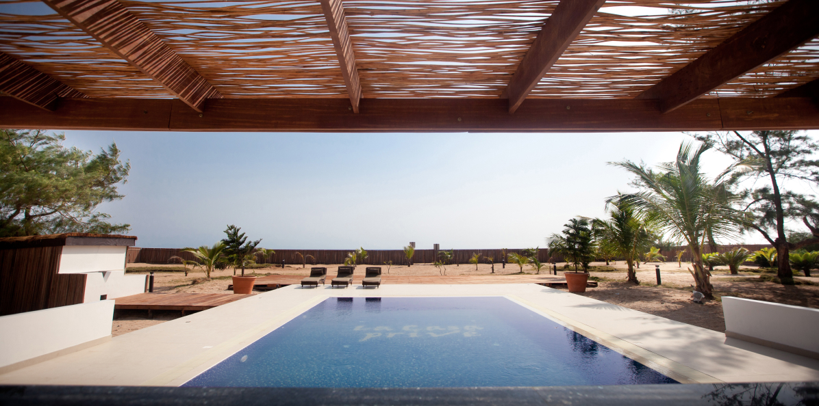 Tranquil poolside retreat with a view of arid landscape and palm trees, under a rustic pergola, designed by Oshinowo Studio, a leading architectural design studio in Lagos.