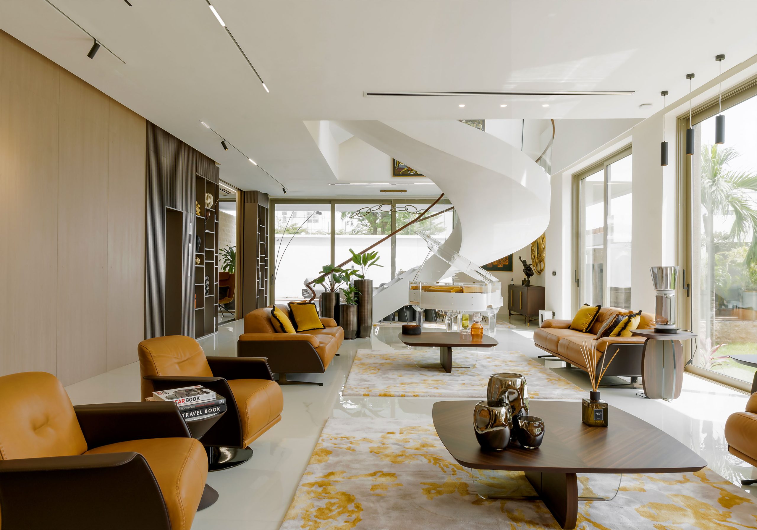 Interior view of a sophisticated living space with modern furniture and a white grand piano, designed by the leading architectural design studio in Lagos, Oshinowo Studio, featuring a spiral staircase, floor-to-ceiling windows that provide ample natural light, and a luxurious marble floor with an abstract patterned rug. This project was led by Tosin Oshinowo.