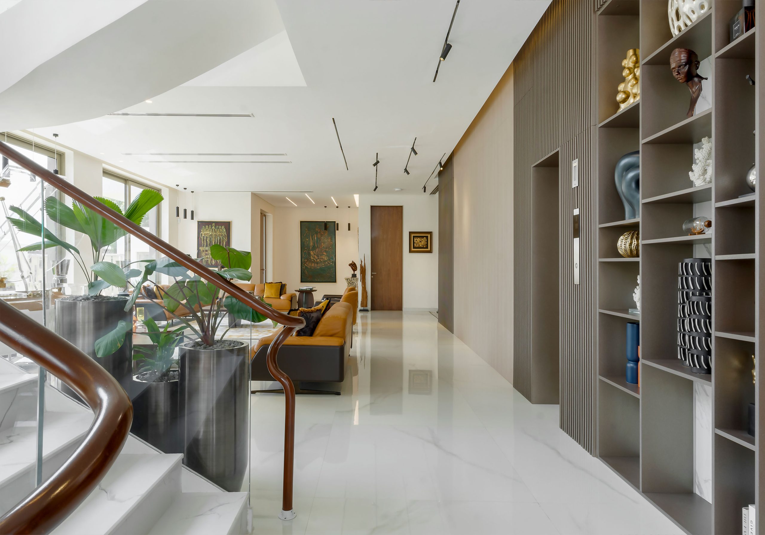 A spacious and bright corridor with a sleek, modern design by the leading architectural design studio in Lagos, Oshinowo Studio, led by Tosin Oshinowo, featuring a glossy marble floor, contemporary furniture, an assortment of plants, decorative shelving with artistic objects, and a warm, inviting living area at the far end. The project was led by Tosin Oshinowo.